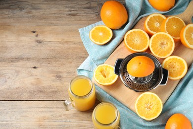 Photo of Freshly squeezed orange juice, fruits, juicer and towel on wooden table, flat lay. Space for text