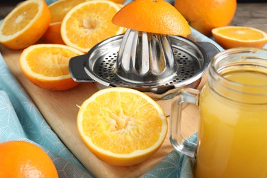 Photo of Freshly squeezed orange juice, fruits, juicer and towel on wooden table, closeup