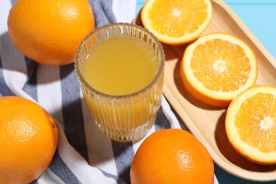 Photo of Freshly squeezed orange juice, fruits and towel on blue wooden table, closeup