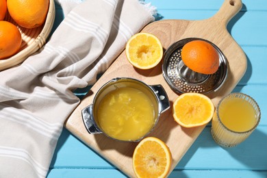 Photo of Freshly squeezed orange juice, fruits and juicer on blue wooden table, flat lay