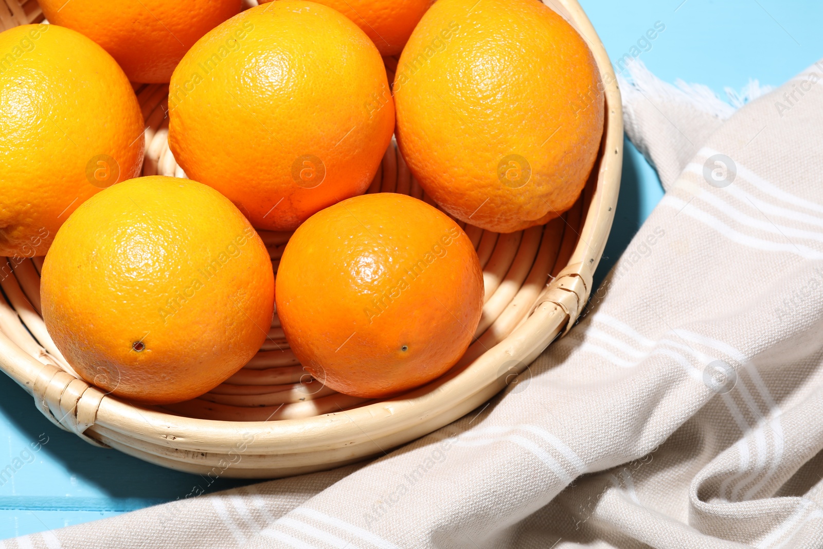 Ripe oranges in basket and towel on blue wooden table, closeup Photo of Ripe oranges in basket and towel on blue wooden table, closeup