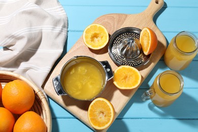 Photo of Freshly squeezed orange juice, fruits, juicer and towel on blue wooden table, flat lay