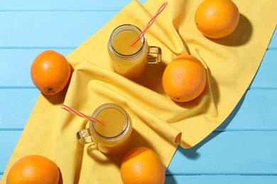 Photo of Freshly squeezed orange juice, fruits and towel on blue wooden table, flat lay