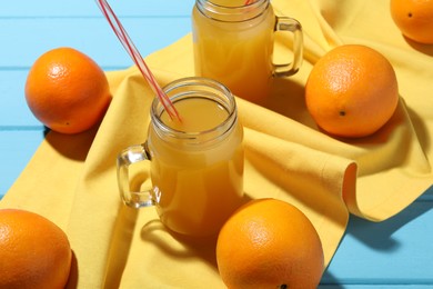 Photo of Freshly squeezed orange juice, fruits and towel on blue wooden table, closeup