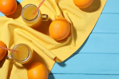 Photo of Freshly squeezed orange juice, fruits and towel on blue wooden table, flat lay