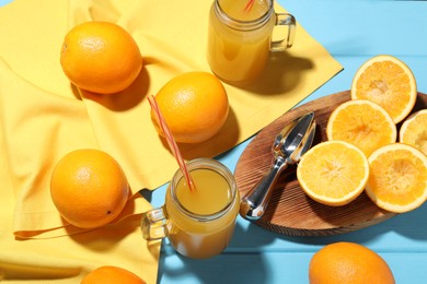 Photo of Freshly squeezed orange juice, fruits, juicer and towel on blue wooden table, above view