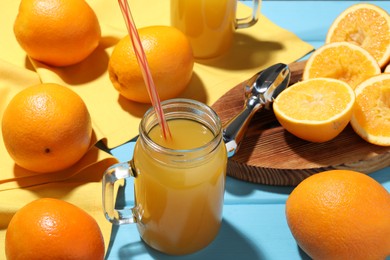 Photo of Freshly squeezed orange juice, fruits and juicer on blue wooden table, closeup