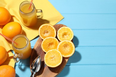 Photo of Freshly squeezed orange juice, fruits, juicer and towel on blue wooden table, flat lay. Space for text