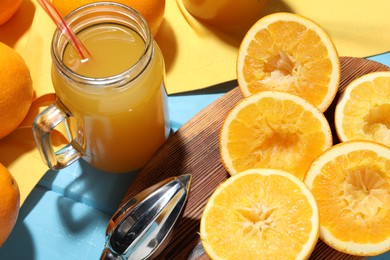 Photo of Freshly squeezed orange juice, fruits and juicer on blue wooden table, closeup