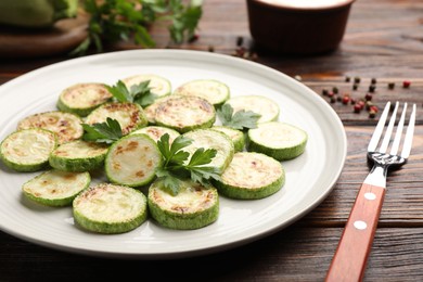 Photo of Delicious fried courgette slices with parsley served on wooden table, closeup