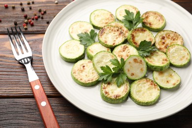 Photo of Delicious fried courgette slices with parsley served on wooden table, closeup