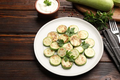 Photo of Delicious fried courgette slices with parsley served on wooden table, closeup