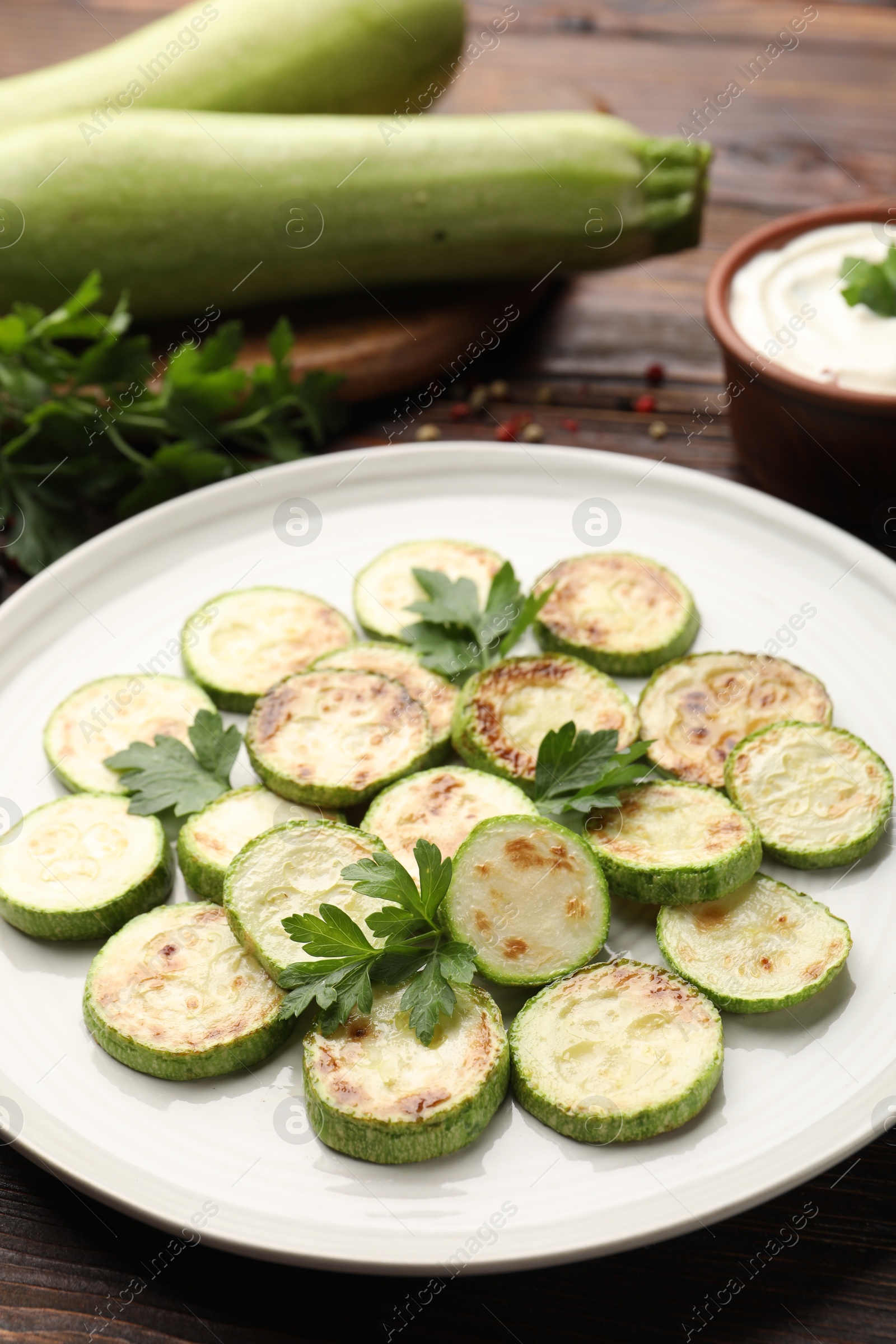 Delicious fried courgette slices with parsley, sour cream and fresh vegetables on wooden table, closeup Photo of Delicious fried courgette slices with parsley, sour cream and fresh vegetables on wooden table, closeup