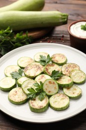 Photo of Delicious fried courgette slices with parsley, sour cream and fresh vegetables on wooden table, closeup