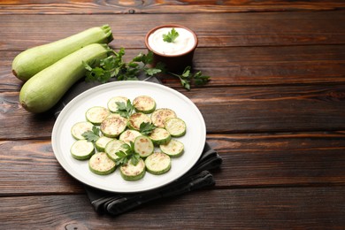 Photo of Delicious fried courgette slices with parsley served on wooden table, closeup. Space for text