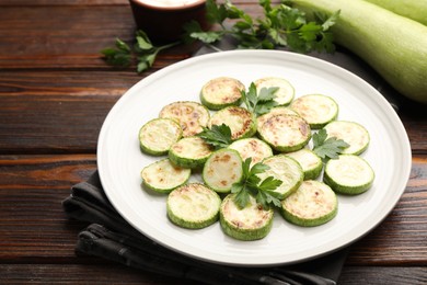 Photo of Delicious fried courgette slices with parsley on wooden table, closeup