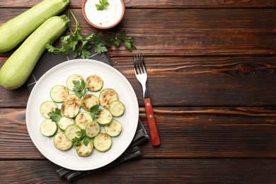 Photo of Delicious fried courgette slices with parsley served on wooden table, flat lay. Space for text
