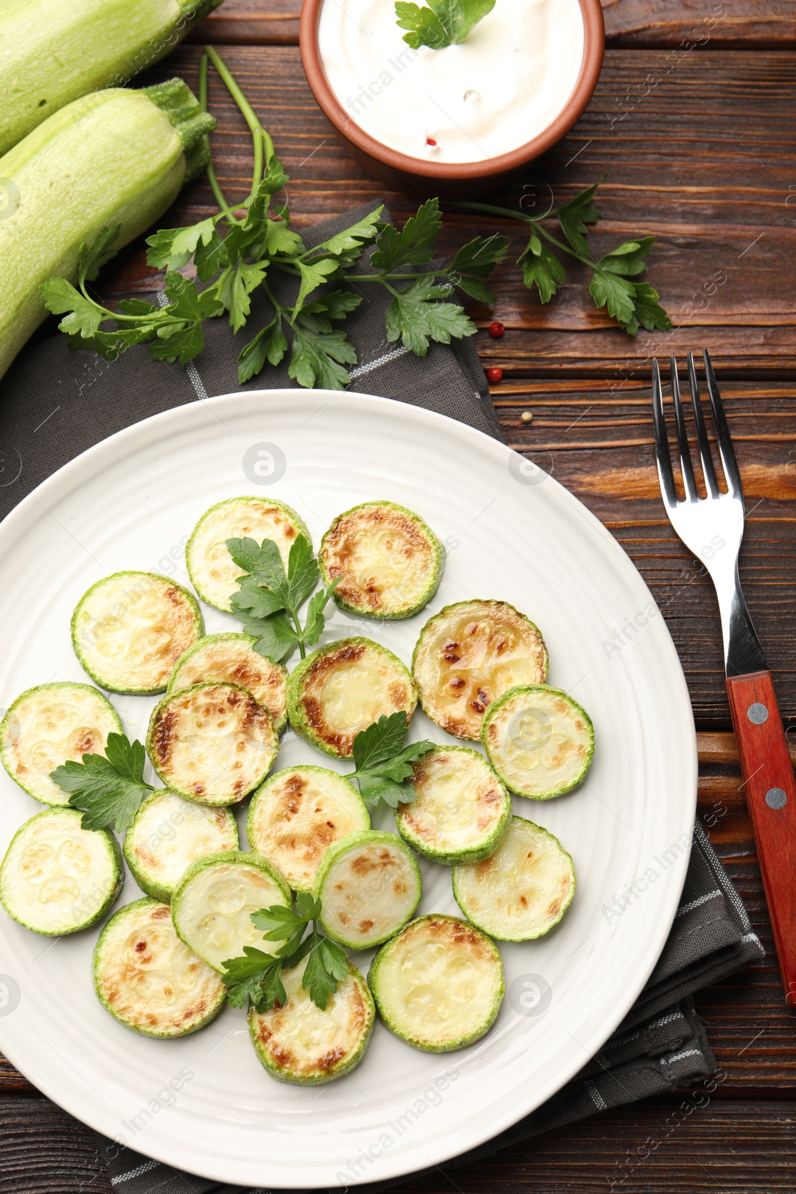 Delicious fried courgette slices with parsley served on wooden table, flat lay Photo of Delicious fried courgette slices with parsley served on wooden table, flat lay