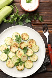 Photo of Delicious fried courgette slices with parsley served on wooden table, flat lay