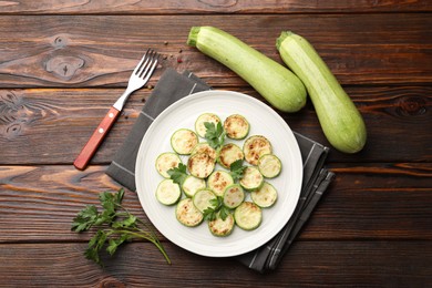 Photo of Delicious fried courgette slices with parsley served on wooden table, flat lay
