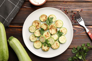 Photo of Delicious fried courgette slices with parsley served on wooden table, flat lay
