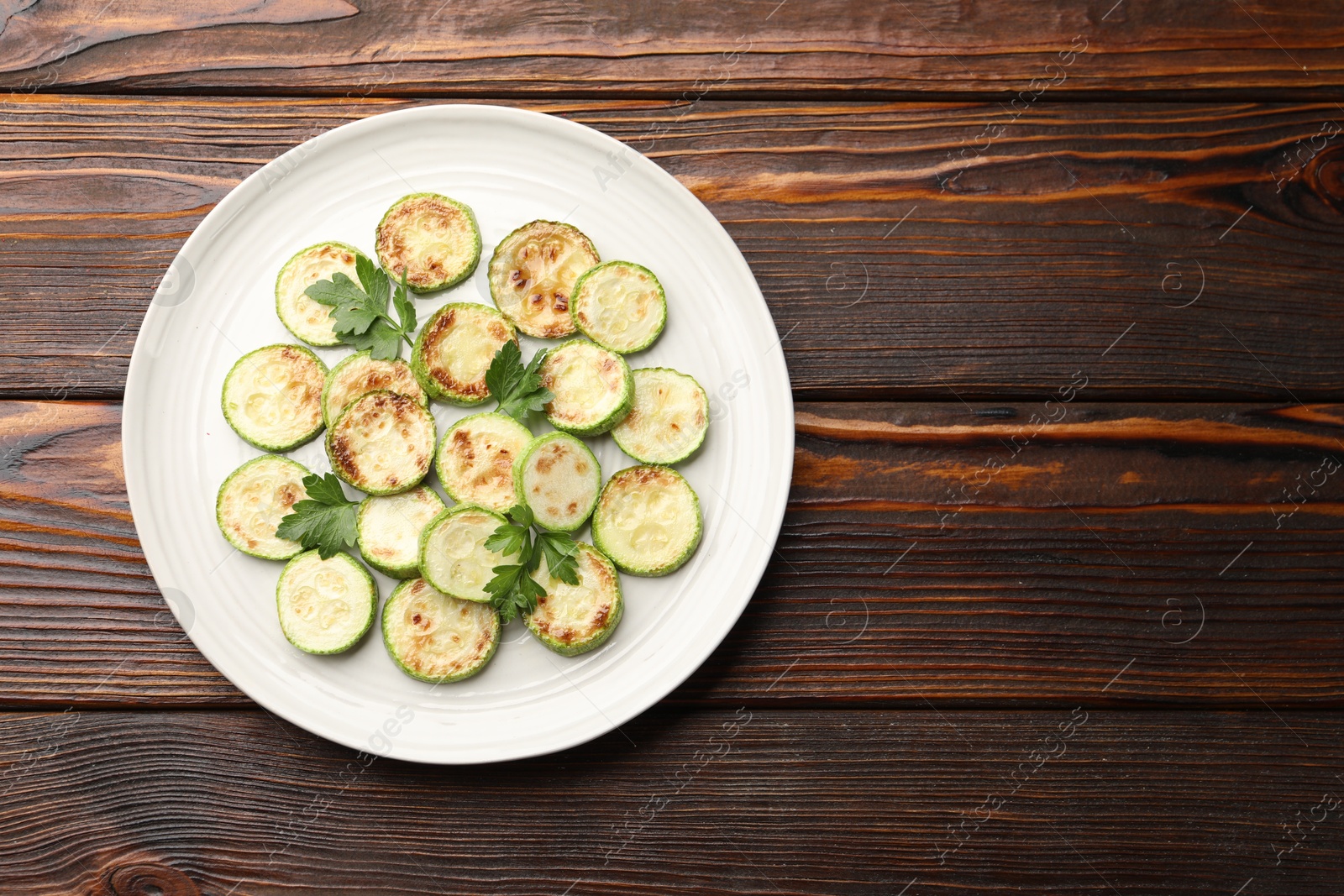 Delicious fried courgette slices with parsley on wooden table, top view. Space for text Photo of Delicious fried courgette slices with parsley on wooden table, top view. Space for text