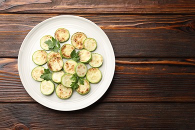 Photo of Delicious fried courgette slices with parsley on wooden table, top view. Space for text