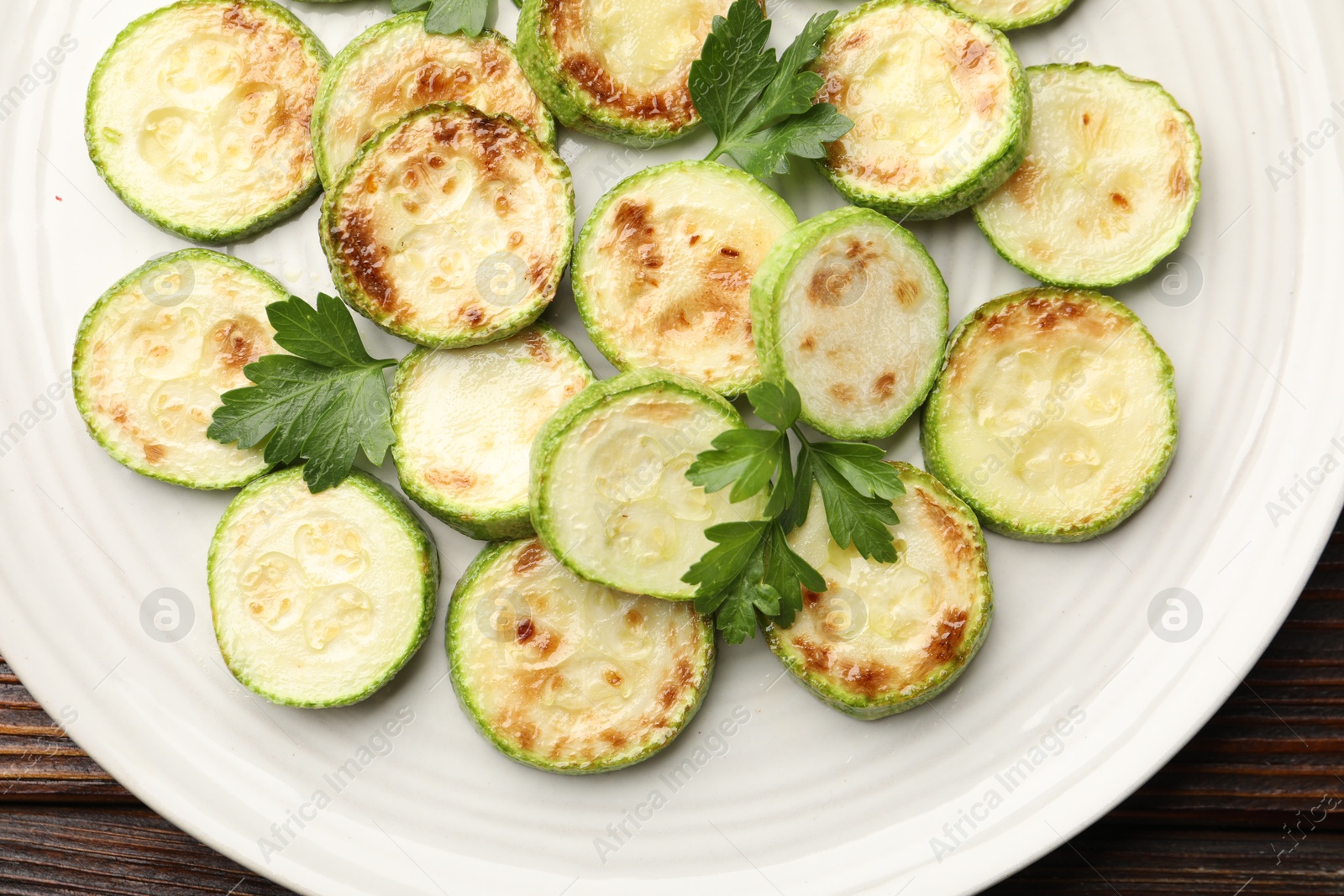 Delicious fried courgette slices with parsley on wooden table, top view Photo of Delicious fried courgette slices with parsley on wooden table, top view