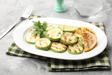 Photo of Delicious fried courgette slices with lemon and parsley served on grey table, closeup
