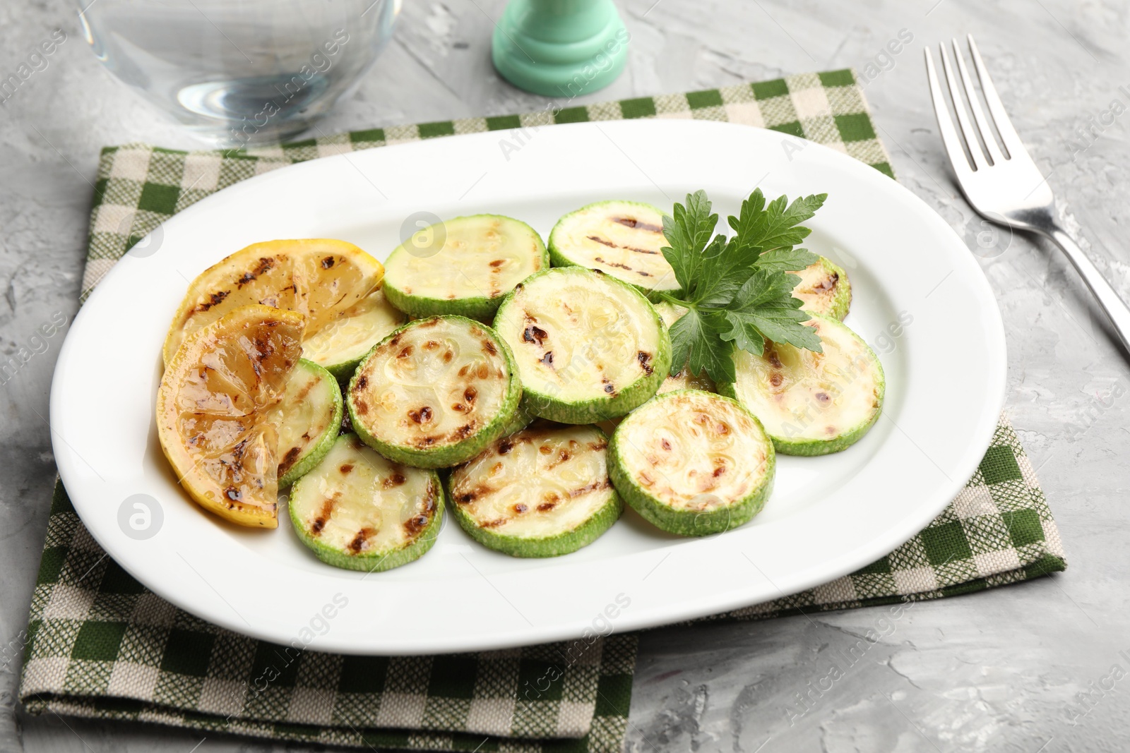 Delicious fried courgette slices with lemon and parsley served on grey table, closeup Photo of Delicious fried courgette slices with lemon and parsley served on grey table, closeup