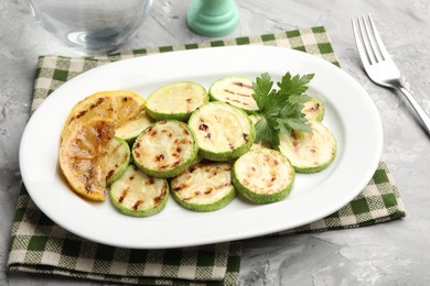 Photo of Delicious fried courgette slices with lemon and parsley served on grey table, closeup
