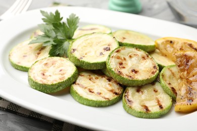 Photo of Delicious fried courgette slices with lemon and parsley on table, closeup
