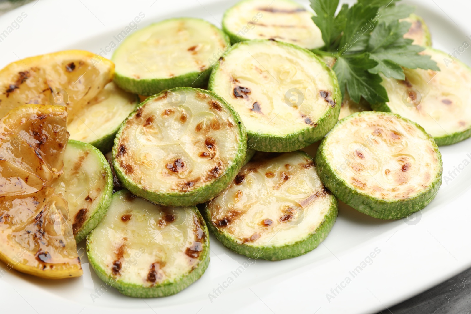 Delicious fried courgette slices with lemon and parsley on table, closeup Photo of Delicious fried courgette slices with lemon and parsley on table, closeup