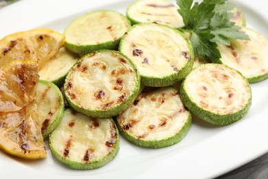 Photo of Delicious fried courgette slices with lemon and parsley on table, closeup