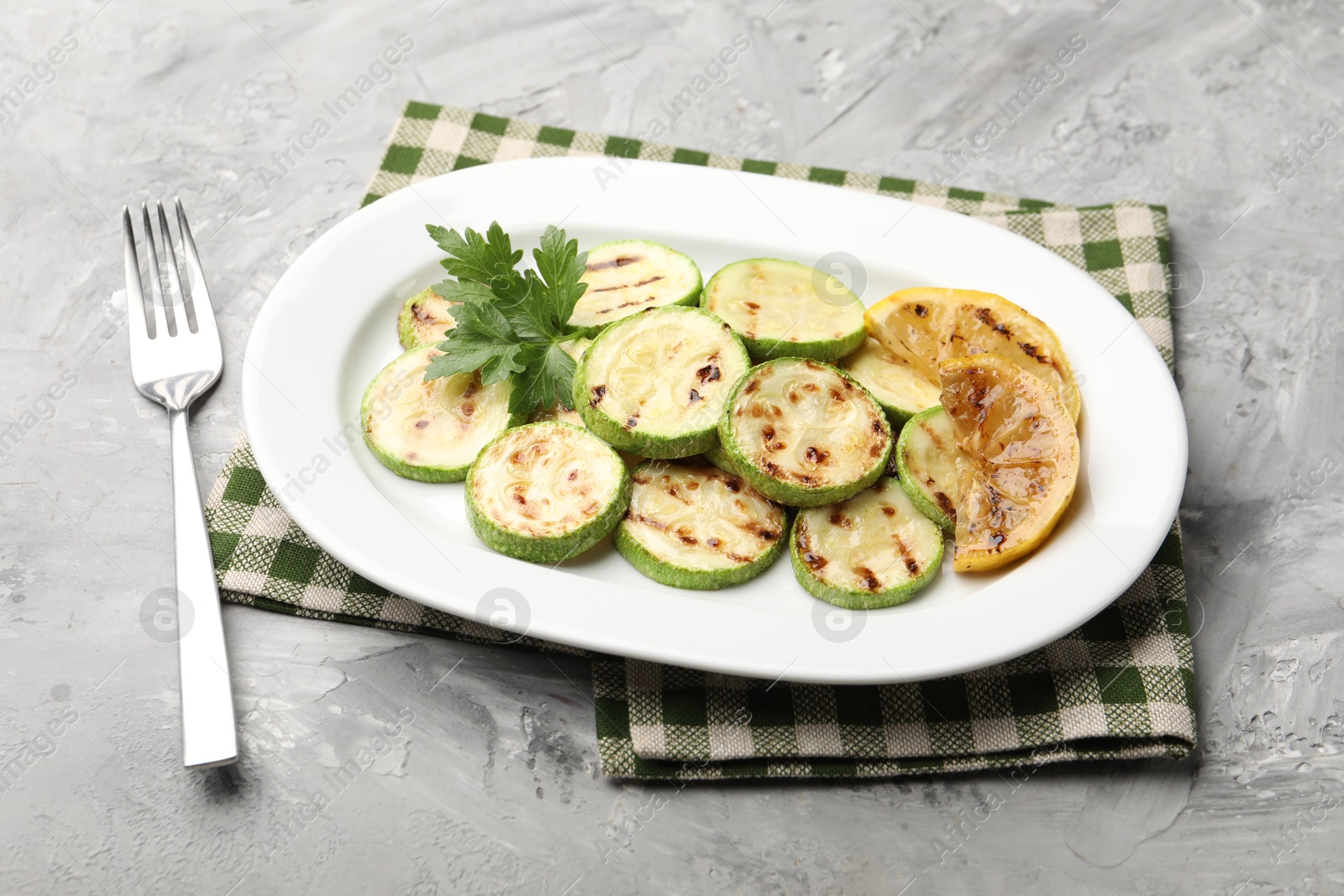 Delicious fried courgette slices with lemon and parsley served on grey table, closeup Photo of Delicious fried courgette slices with lemon and parsley served on grey table, closeup