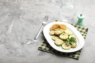 Photo of Delicious fried courgette slices with lemon and parsley served on grey table. Space for text