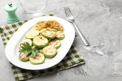 Photo of Delicious fried courgette slices with lemon and parsley served on grey table, closeup. Space for text