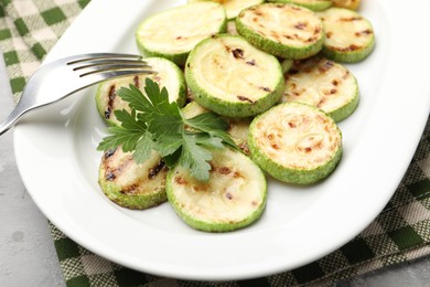 Photo of Delicious fried courgette slices with parsley on grey table, closeup