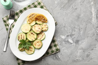 Photo of Delicious fried courgette slices with lemon and parsley served on grey table, flat lay. Space for text