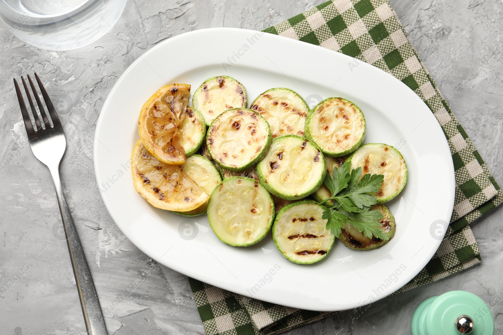 Delicious fried courgette slices with lemon and parsley served on grey table, flat lay Photo of Delicious fried courgette slices with lemon and parsley served on grey table, flat lay