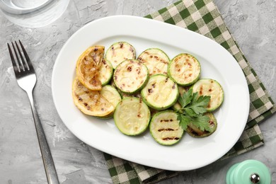 Photo of Delicious fried courgette slices with lemon and parsley served on grey table, flat lay