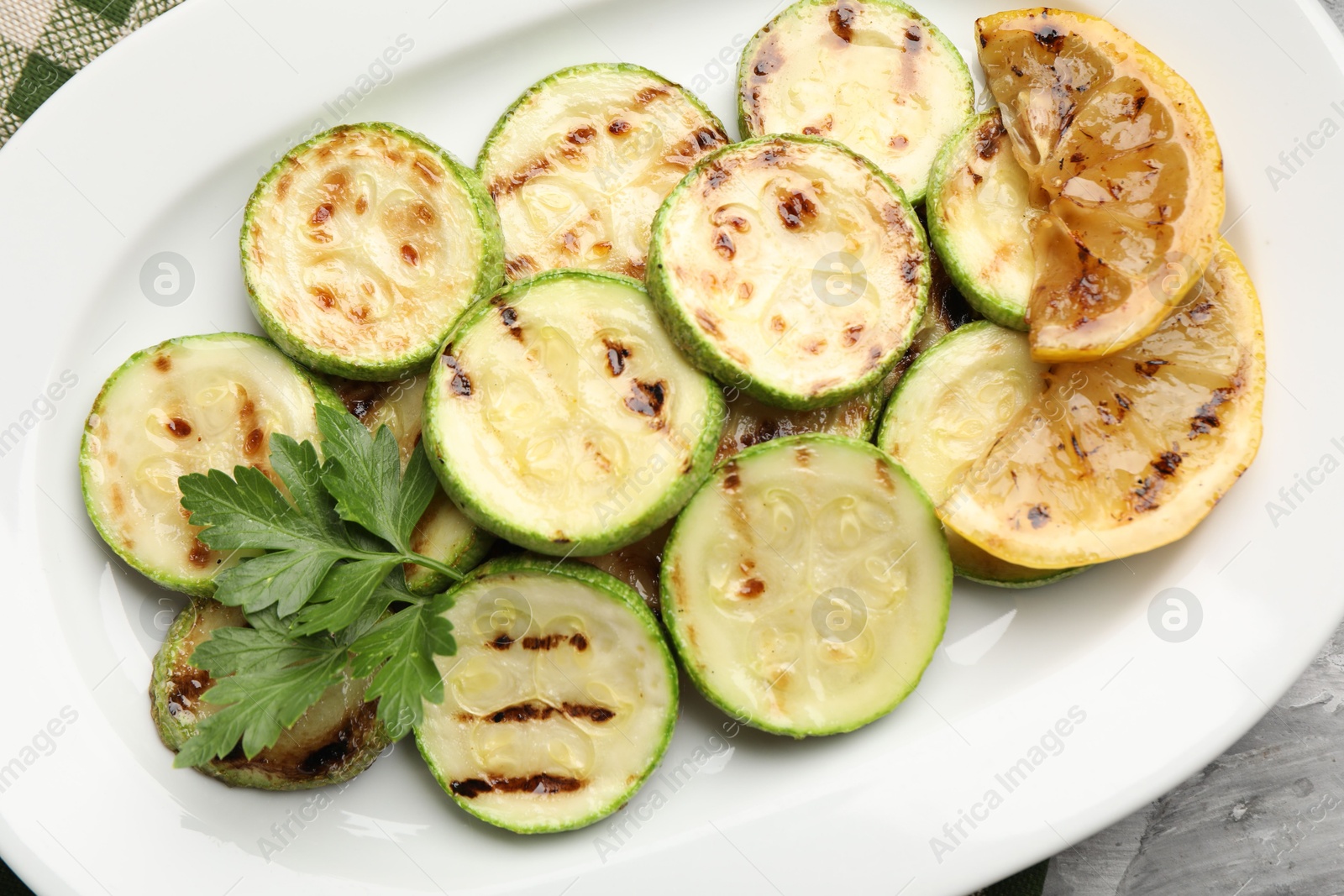 Delicious fried courgette slices with lemon and parsley on grey table, top view Photo of Delicious fried courgette slices with lemon and parsley on grey table, top view