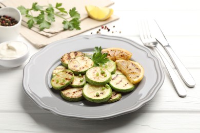 Photo of Delicious fried courgette slices with lemon and parsley served on white wooden table, closeup