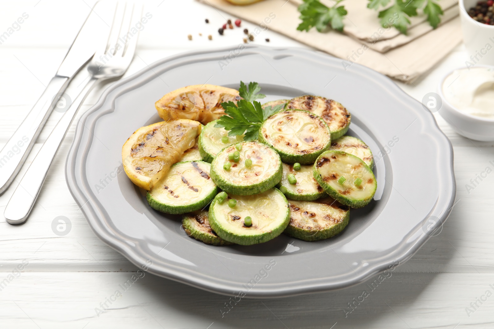Delicious fried courgette slices with lemon, green onion and parsley served on white wooden table, closeup Photo of Delicious fried courgette slices with lemon, green onion and parsley served on white wooden table, closeup