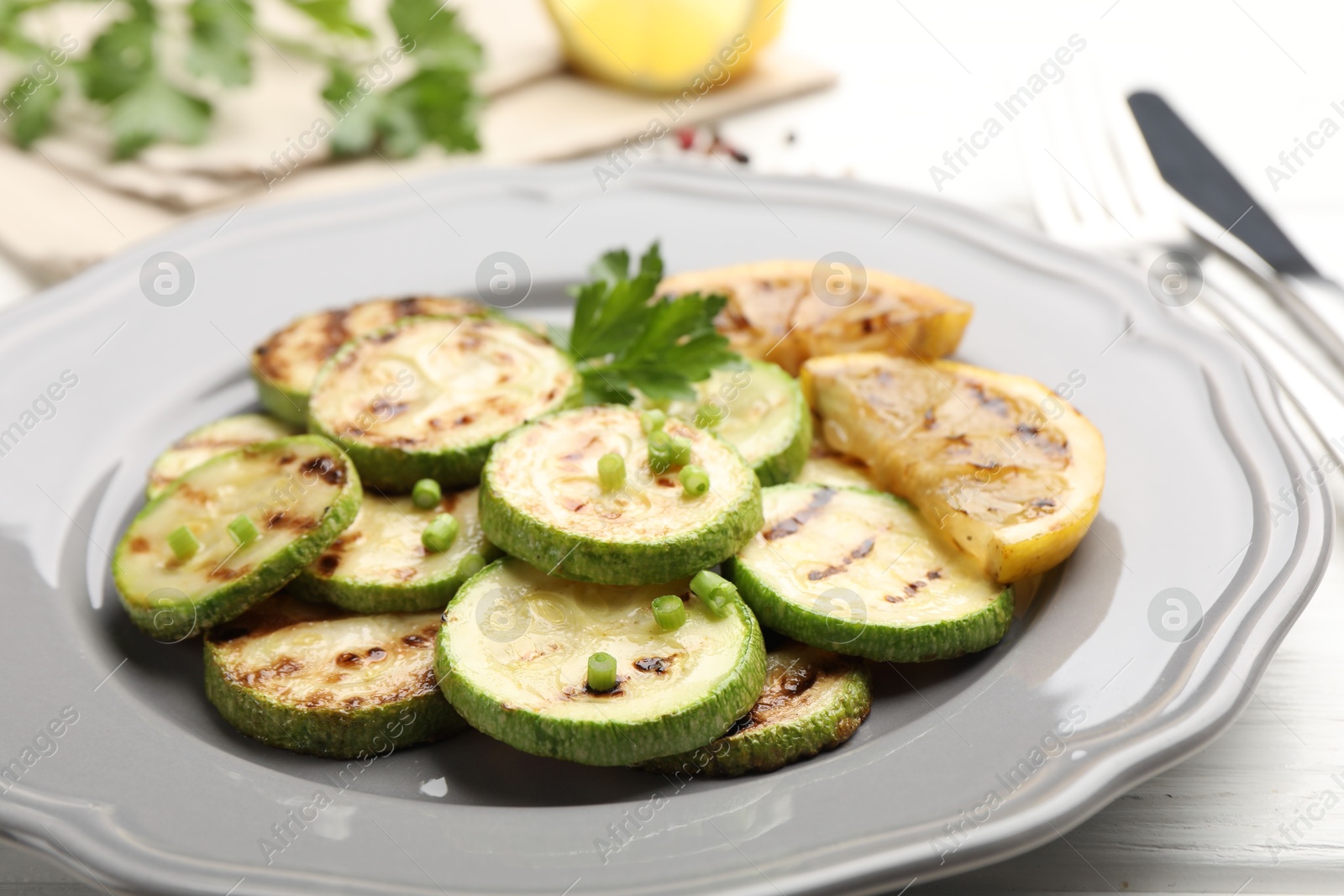 Delicious fried courgette slices with lemon, green onion and parsley on white wooden table, closeup Photo of Delicious fried courgette slices with lemon, green onion and parsley on white wooden table, closeup