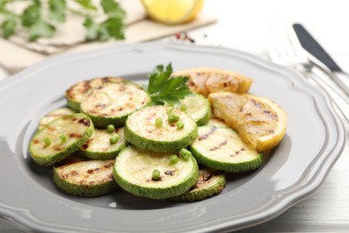 Photo of Delicious fried courgette slices with lemon, green onion and parsley on white wooden table, closeup
