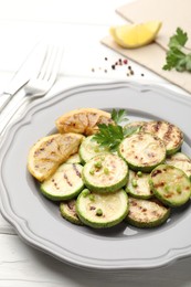 Photo of Delicious fried courgette slices with lemon and parsley served on white wooden table, closeup