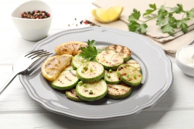 Photo of Delicious fried courgette slices with lemon and parsley served on white wooden table, closeup