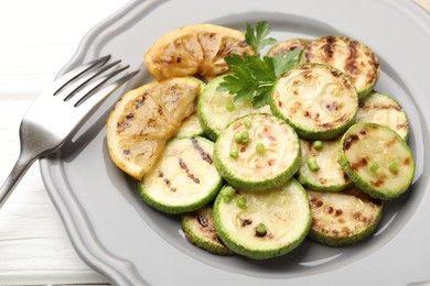 Photo of Delicious fried courgette slices with lemon, green onion and parsley on white wooden table, closeup