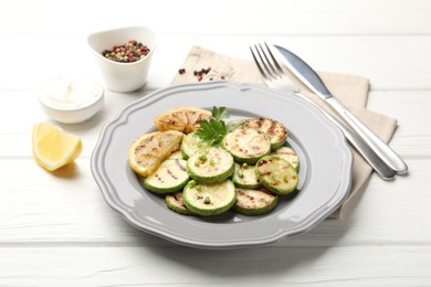 Photo of Delicious fried courgette slices with lemon and parsley served on white wooden table, closeup
